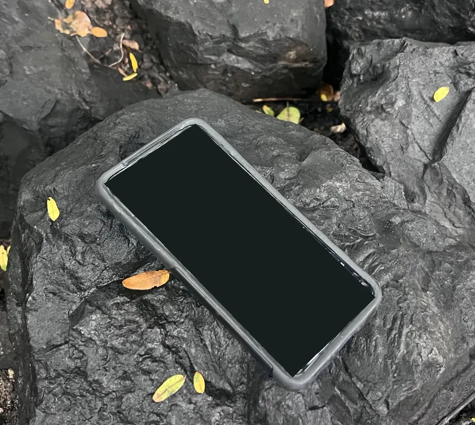 My phone-based cyberdeck on dark rocks beside yellow leaves, with the map display covered for location privacy.