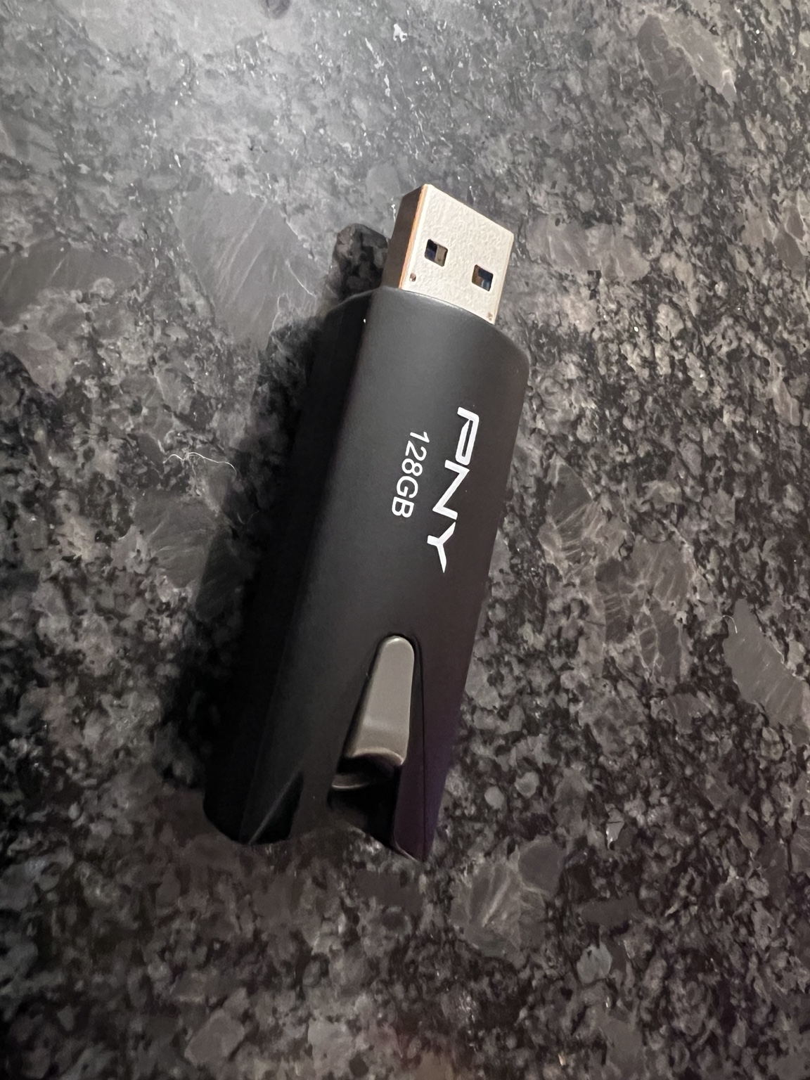 My black PNY USB flash drive with its 128GB label, sliding housing, and USB-A connector visible.
