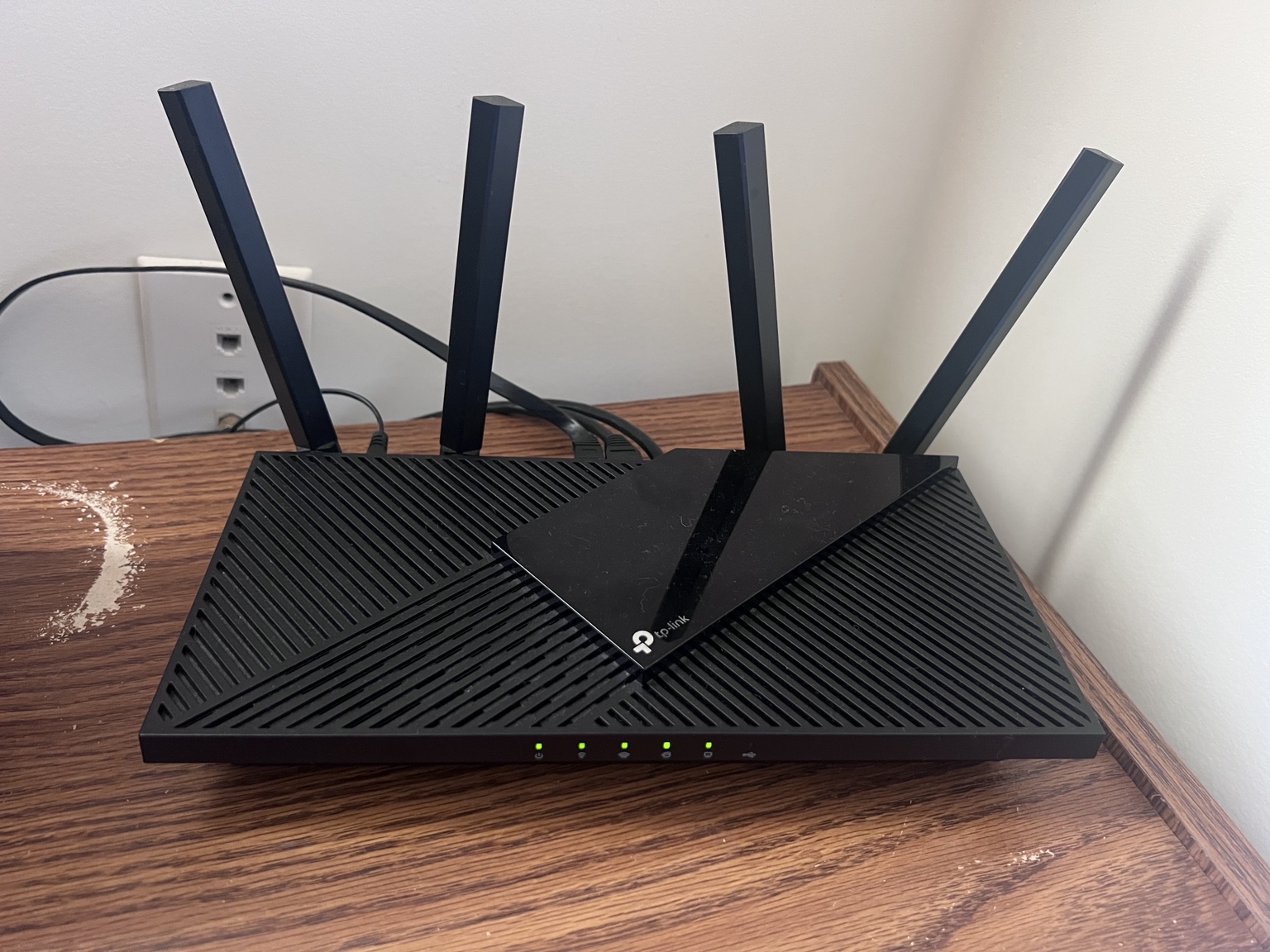 My black TP-Link Archer AX21 router on a wooden shelf, with four upright antennas and green status lights.