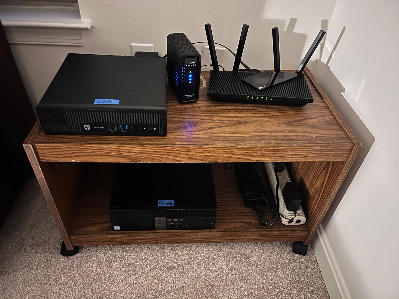 My actual home lab: two repurposed computers on a wooden shelf, with a modem, router, and power connections.